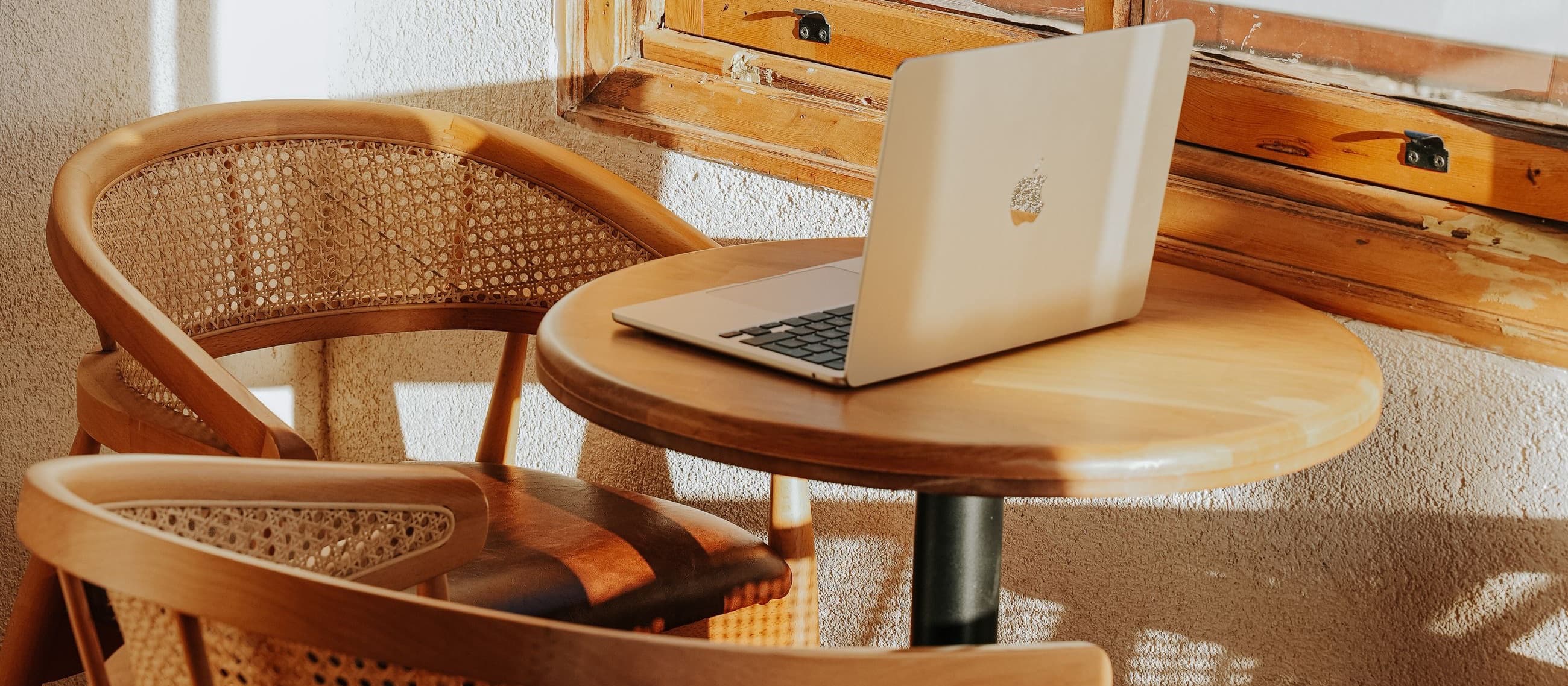 Cane armchairs and a laptop on a small wooden table in warm afternoon light