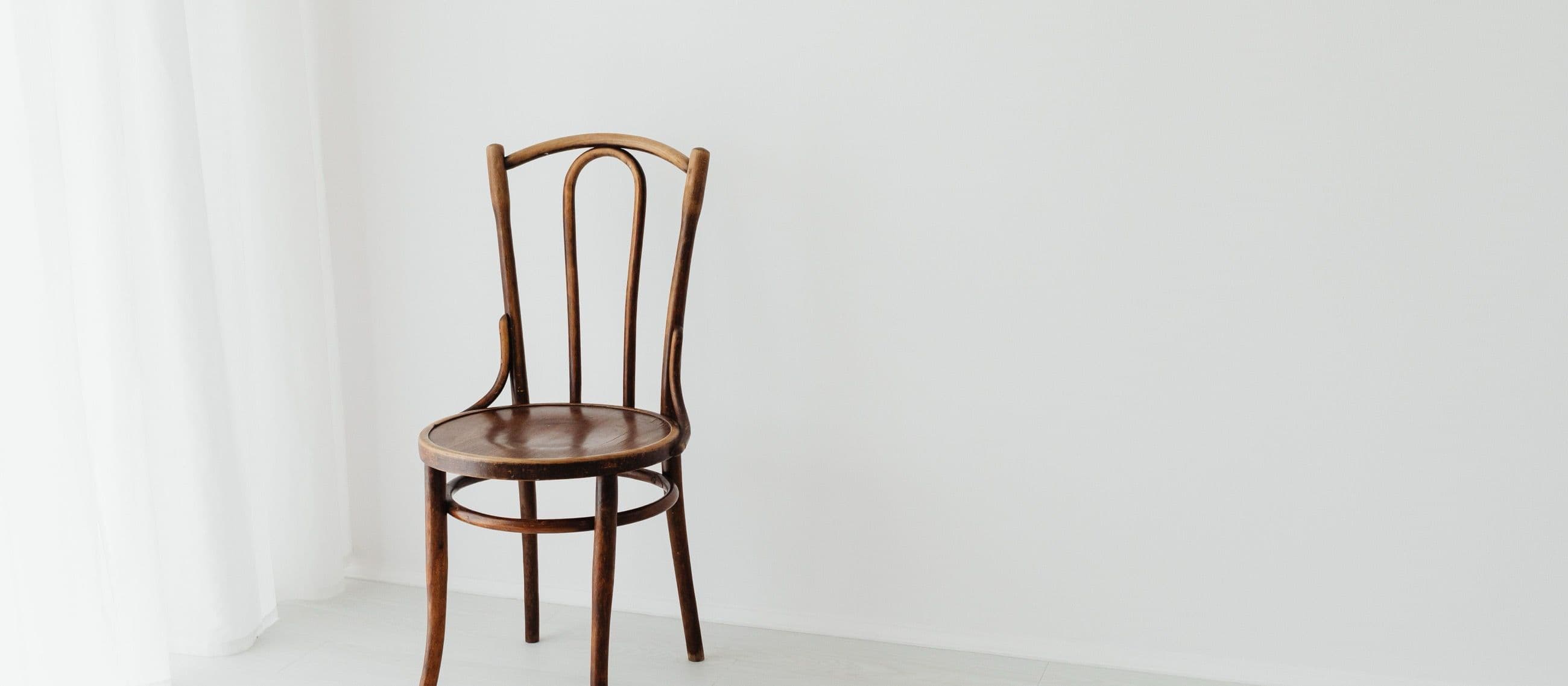 A single bentwood wooden chair beside a sheer white curtain against a soft white wall