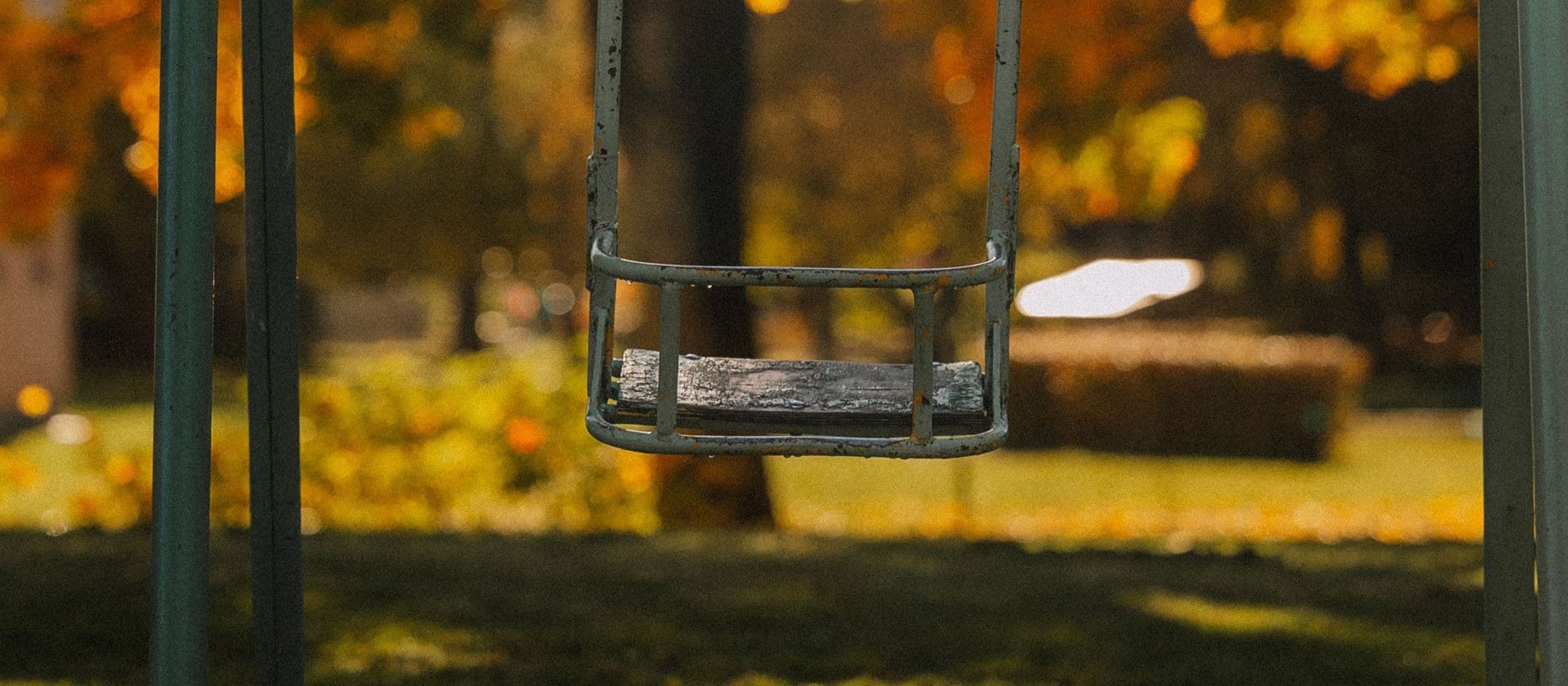 An empty swing hanging in a park framed by golden autumn foliage