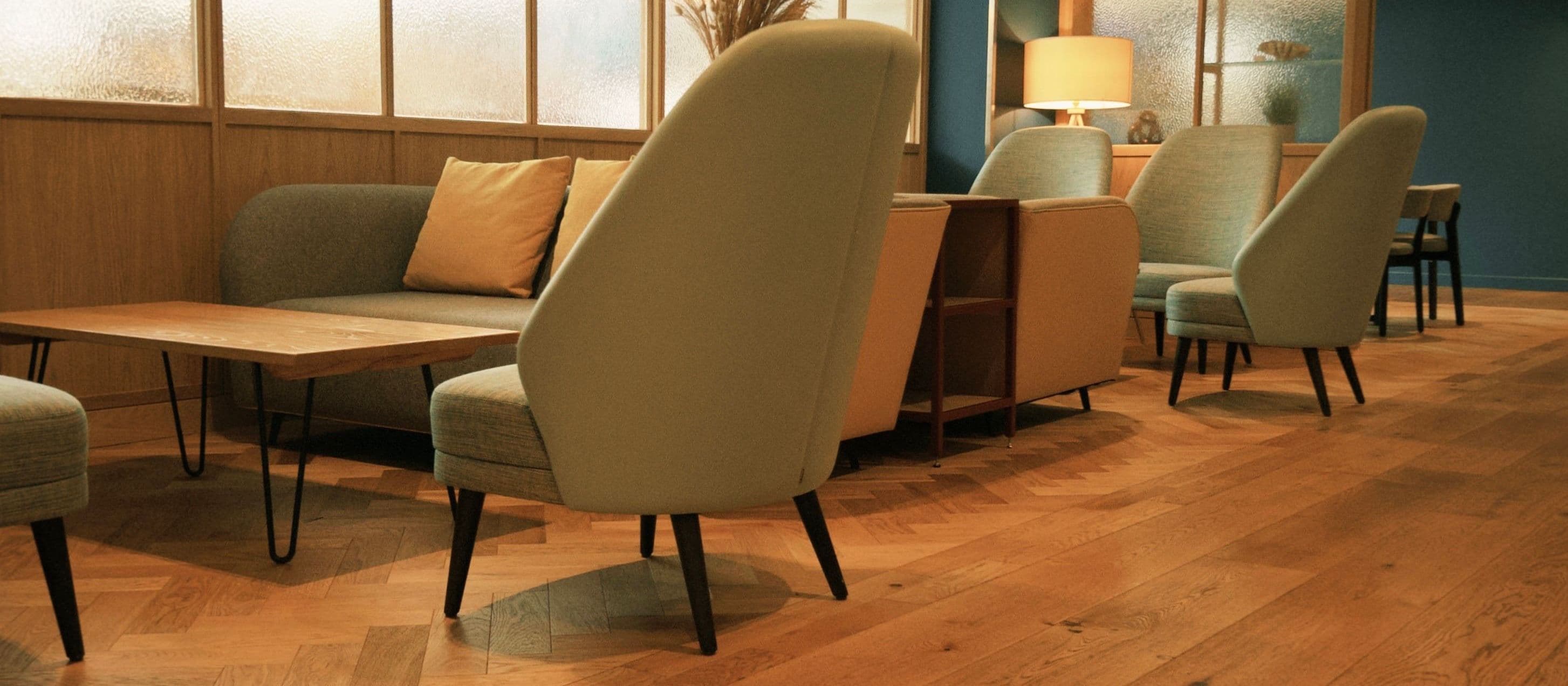 A warm lounge with a sofa and several armchairs arranged together on a herringbone wood floor